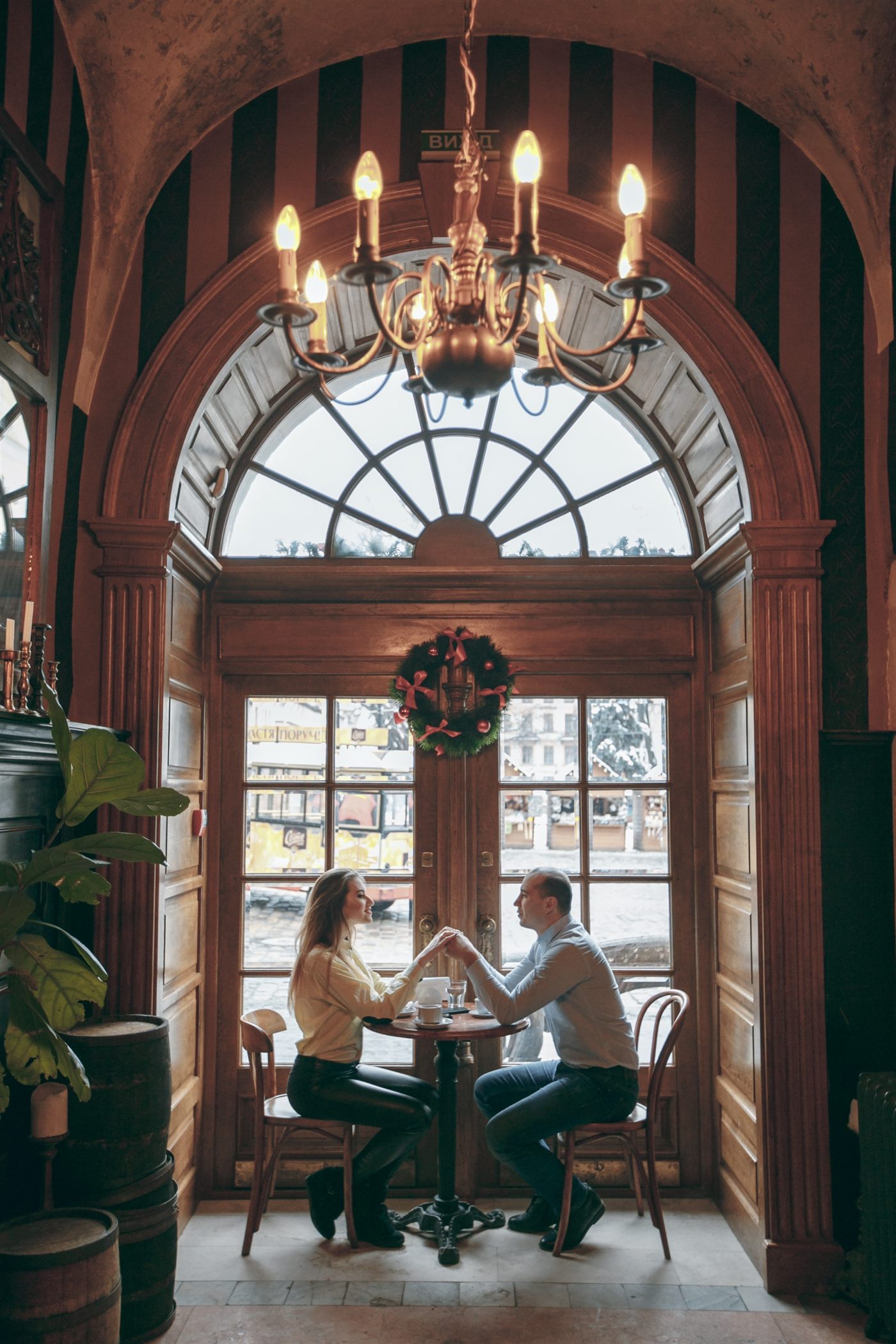 A couple holding hands at a café table beneath an arched window